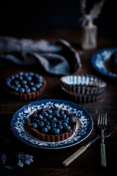 two blueberry tarts sitting on top of a table next to a fork and cupcake tins