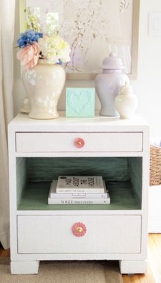 a white nightstand with flowers and books on it