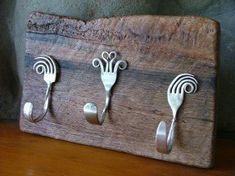 three spoons and two forks are mounted to a wooden board with hooks on it