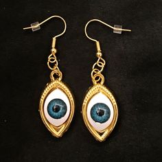 "This is a pair of gold earrings with eerily realistic blue glass eyeballs, that seem to always be looking at you. They are a really fun and a little spooky! Hung on fish hook ear wires, they are 2\" long, and just over 1/2\" wide. Make sure to check out my shop for more hair pins, jewelry, earrings, accessories, and all sorts of fun stuff!" Novelty Gold Metal Jewelry, Handmade Gold Novelty Jewelry, Gold Novelty Jewelry For Party, Earrings Blue Eyes, Novelty Drop Earrings, Gold Novelty Earrings For Gifts, Novelty Gold Dangle Jewelry, Gold Novelty Pierced Earrings, Novelty Metal Earrings With Ear Wire