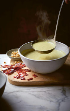 a bowl of soup being spooned into it with bacon on the side next to other bowls