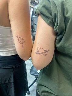 two women with matching tattoos on their arms, one is holding the other's arm