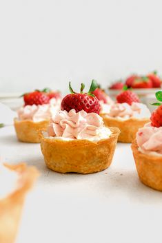 several mini pies with strawberries and whipped cream on top are sitting on a table