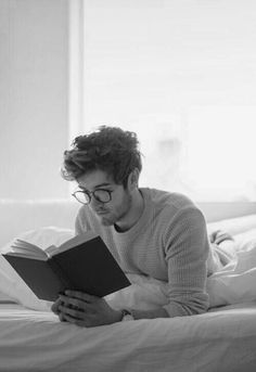 a man laying in bed reading a book