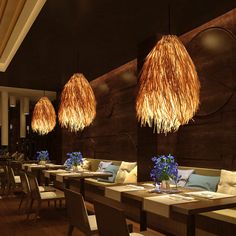 an empty restaurant with tables and chairs in front of large wall hangings that have straw lamps above them