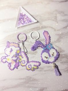 two cross stitch keychains are sitting on a marble surface with a triangle in the background