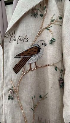 a bird is sitting on the branch of a tree embroidered onto a jacket with writing