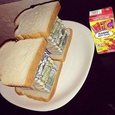 two sandwiches on a white plate with money in between them and a box of candy