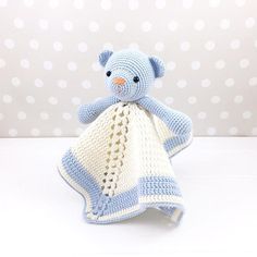 a crocheted blue teddy bear wrapped in a blanket on a white surface with polka dots