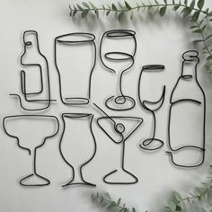 a bunch of wine glasses and bottles on a white wall with green leaves around them