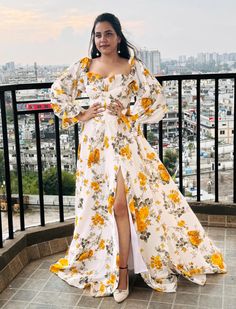 This stunning floral long gown features a vibrant, romantic design perfect for any special occasion. The dress boasts a captivating white base adorned with a beautiful yellow and green floral print, giving it a fresh, summery appeal. The gown's off-shoulder design, complemented by puffed, voluminous sleeves, adds a touch of vintage elegance while accentuating the neckline and shoulders gracefully. The corset-style bodice cinches at the waist, enhancing the silhouette and creating a flattering hourglass shape. The skirt flows effortlessly from the waist down, featuring a high slit that adds a hint of allure and movement to the overall look. The flowing, floor-length hemline ensures a dramatic and eye-catching effect as it gently brushes the ground, making the wearer feel like a modern-day p Fitted White Floral Print Gown, Yellow A-line Maxi Dress For Wedding, Maxi Length Gown With Fitted Bodice For Garden Party, Yellow Floral Print Dress For Wedding, White Floral Print Party Gown, Floral Print A-line Maxi Dress For Wedding, Floral Print A-line Wedding Gown, Floral Print Maxi Dress For Wedding, Floral Print Maxi Gown For Garden Party