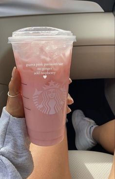 a woman holding up a pink starbucks cup