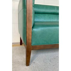 a green leather chair sitting in front of a white brick wall with wood trimming