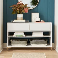 a white shelf with baskets and plants on it in front of a blue painted wall