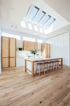 an open kitchen with wooden flooring and skylights above the countertop, along with bar stools