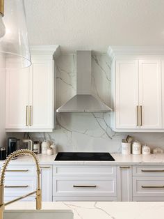 a kitchen with white cabinets and marble counter tops, gold handles on the faucet