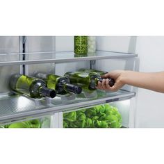 a person is opening the refrigerator door to see what's inside it and holding two wine bottles in their hand