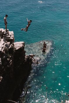 three people jumping off rocks into the ocean from a cliff in front of some water