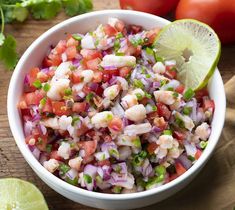 a close up of a bowl of food on a table with limes and tomatoes