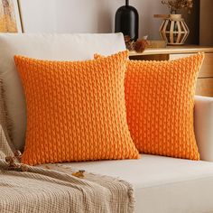 two orange pillows sitting on top of a white couch