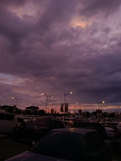 cars are parked in a parking lot at dusk with the sun going down and dark clouds above them