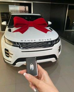 a person holding a cell phone in front of a white car with a red bow on it