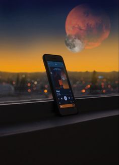 a cell phone sitting on top of a window sill in front of a sunset