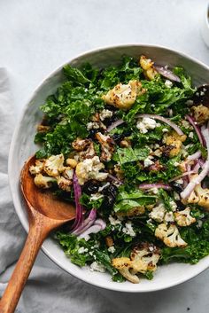 a white bowl filled with greens and cauliflower on top of a wooden spoon