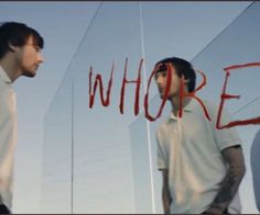 two men standing next to each other in front of a glass wall with the word who? written on it