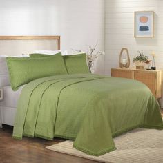 a bed with green bedspread and pillows in a white room next to a night stand