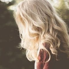 the back of a woman's head with long blonde hair in front of trees