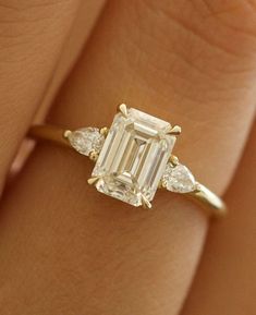 a woman's hand holding an emerald and diamond ring