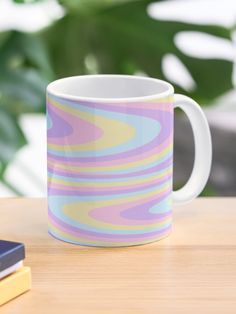 a colorful coffee mug sitting on top of a wooden table next to a cell phone