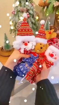 someone is holding two teddy bears in their hands with christmas decorations on the table behind them