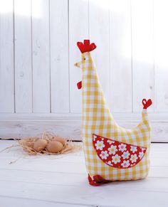 a yellow and white chicken pillow sitting next to an egg in a nest on the floor