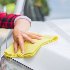 a person wiping the hood of a car with a yellow cloth