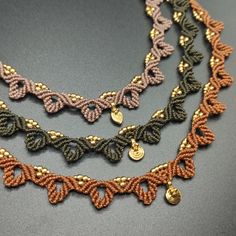 three braided necklaces with gold and brown beads on a gray surface, one has a charm in the middle