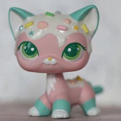 a pink and green cat figurine sitting on top of a wooden table next to a white wall