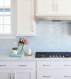 a kitchen with white cabinets and blue backsplash tiles on the wall behind the stove