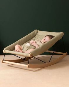 a baby laying in a rocking chair on top of a wooden floor next to a green wall