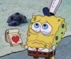 spongebob holding an open book in front of a rock and heart on the ground