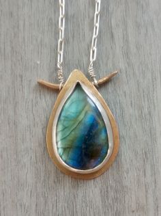 Large blue labradorite teardrop shape cabochon in a bronze and silver bezel setting on long silver chain chain necklace. The gemstone is natural with the gorgeous rainbow colored light flashes that labradorite is famous for: labradorescence. The labradorite  The labradorite stone is about 1 inch long and 0.6 inch wide. The pendant is about 1.25 inches long and about 0.75 inch wide. The necklace will arrive in a simple gift box with hemp flower ribbon, ready as a gift. The necklace is made out of Unique Hand Forged Long Drop Jewelry, Handmade Labradorite Drop Necklaces, Handmade Labradorite Drop Necklace, Silver Brass Teardrop Necklace, Teardrop Shaped Silver Brass Necklace, Handmade Drop-shaped Labradorite Necklaces, Artisan Bronze Teardrop Jewelry, Wire Wrapped Teardrop Brass Necklaces, Unique Hand Forged Teardrop Pendant Jewelry