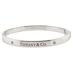 A Tiffany & Co. Diamond bangle, made of 18ct White Gold, and weighing 38.7 gm. Stamped: Tiffany & Co. AU 750. The bangle is set with 2 round, brilliant cut Diamonds, colour D-E and clarity VVS with a total weight of 0.10 ct. Metal: 18ct White Gold Carat: 0.10ct Colour: D-E Clarity: VVS Cut: Round Brilliant Weight: 38.7 grams Engravings/Markings: Signed Tiffany & Co. AU 750. Size/Measurement: Size Medium Current Condition: Excellent - Consistent with age and use. Accompanied by: This Tiffany & Co Tiffany And Co Diamond, Tiffany And Co Bracelet, Tiffany And Co, Diamond Bangle, Hinged Bangle, Brilliant Cut Diamond, Tiffany & Co., Round Brilliant, Hinges