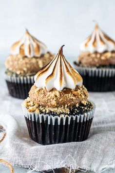 three cupcakes with white frosting and icing on top, sitting on a table