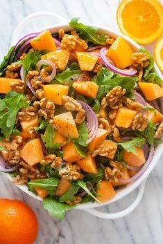 a white bowl filled with salad next to oranges and an orange slice on the side