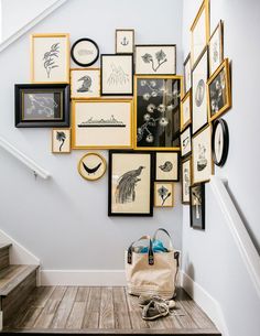 a bunch of framed pictures are hanging on the wall above a stair case with a handbag next to it