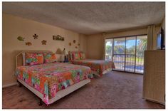 two beds in a room with sliding glass doors leading to an outside deck and palm trees