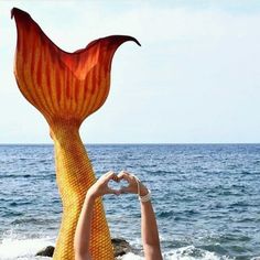 a woman is holding up a large piece of art at the ocean's edge