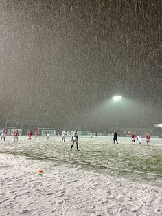 a group of people playing soccer in the snow on a snowy field at night time