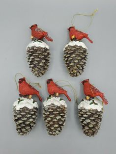 six pine cone ornaments with red cardinals on each ornament, hanging from chains